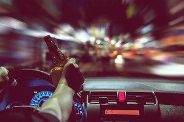 Man drink beer while driving at night in the city dangerously, left hand drive system