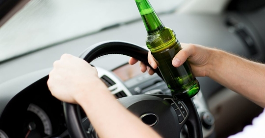 person holding a beer bottle while driving