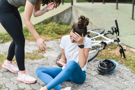Cyclist sitting on pavement holding her head after a bicycle crash, with a fitness tracker on her wrist and a fallen bike nearby, illustrating how ride data and GPS tracking may support accident claims.